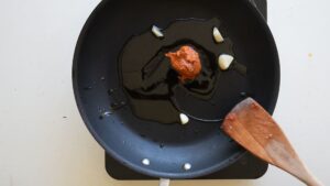 Recette Facile et Authentique de Haricots Verts à l’Italienne avec Tomates - Dans une grande poêle, faites chauffer de l'huile d'olive à feu moyen puis ajoutez les gousses d'ail, coupées en tranches, et faites-les revenir jusqu'à ce qu'elles dégagent leur parfum